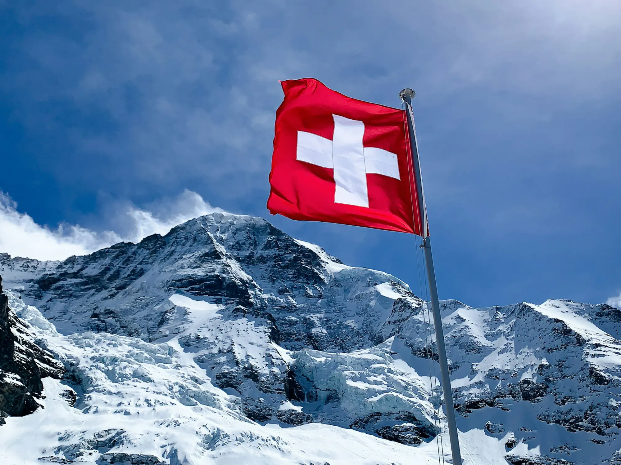 The Swiss flag flying in front of a snow-covered mountain.